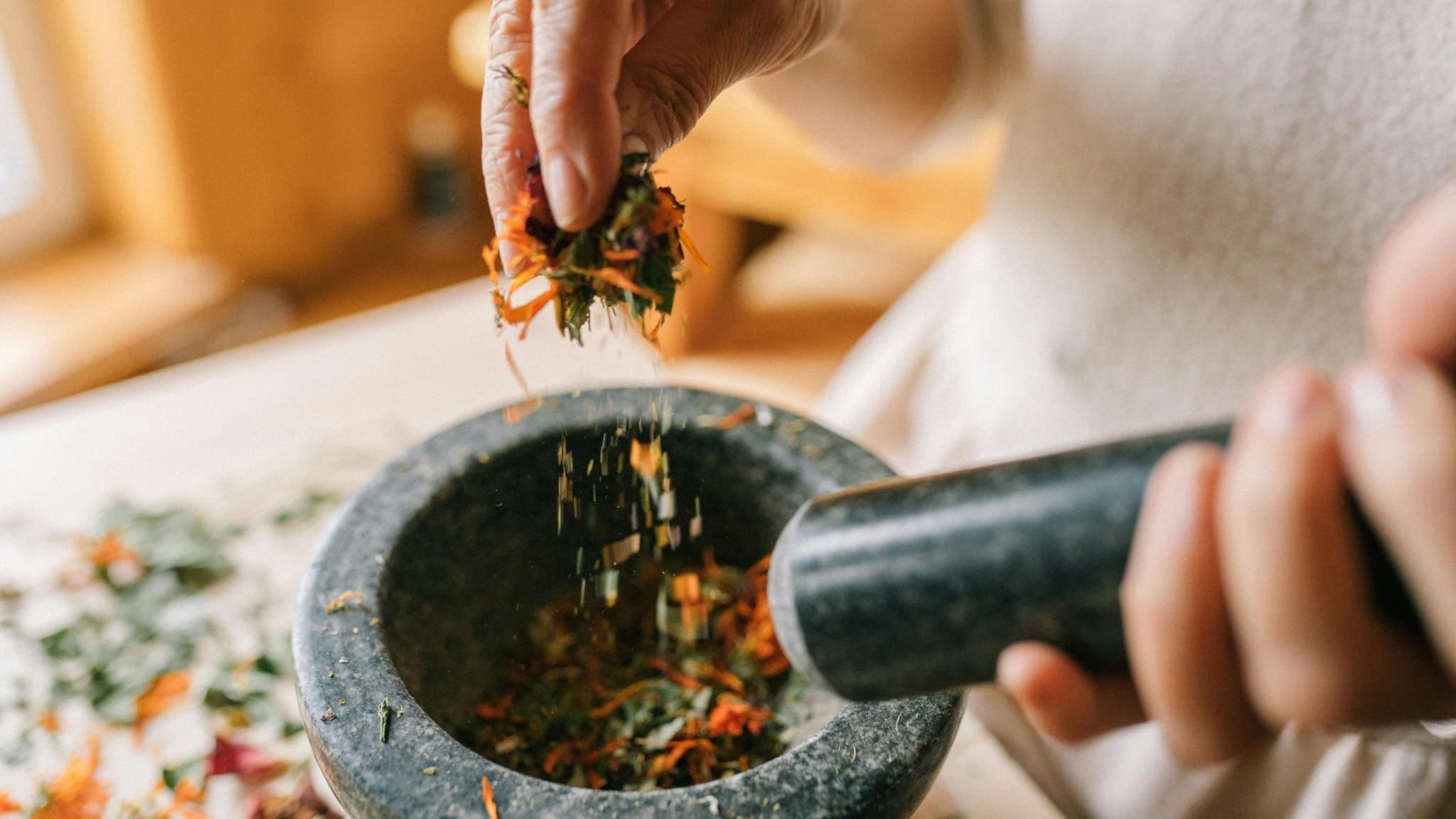 Närbild på händer som bereder örter i en mortel, kopplat till ayurvedisk forskning och alternativ medicin. Fokus ligger på naturliga ingredienser och traditionella metoder för hälsa.