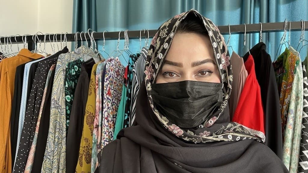 Khadija Muhammadi står framför ett ställ med färgglada afghanska hantverk och klädesplagg på sitt lärcenter.